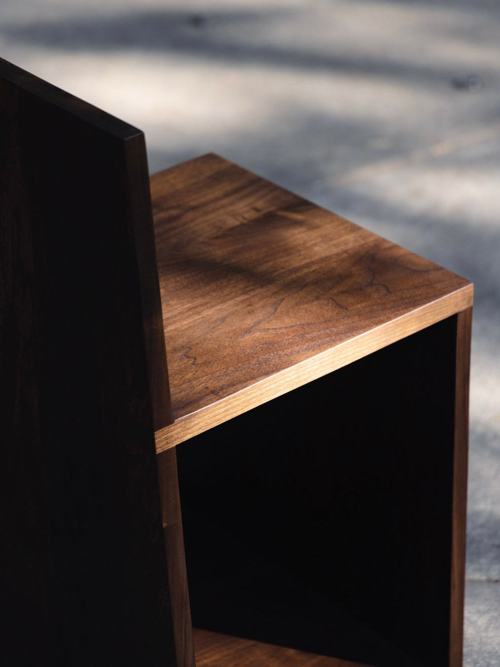 The 'Totem' Chair by Siete Studio is a dark walnut chair with a minimalist, modern design. It features a flat seat, straight angled backrest, and showcases the wood grain and smooth finish, emphasizing its totemic aesthetic.