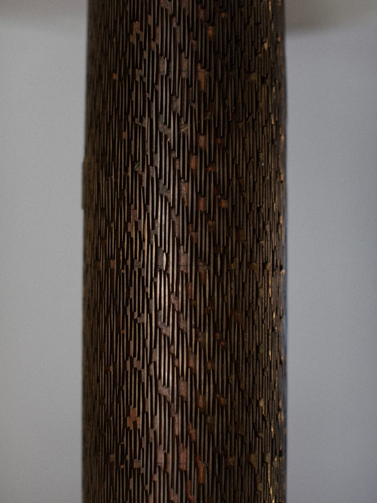 Close-up image of a textured bronze metal surface with a repeating pattern of small, interlocking rectangular shapes. The dark brown coloration and lighting highlight the intricate details, closely resembling the design of Out For Lunch’s Brutalist Floor Lamp.