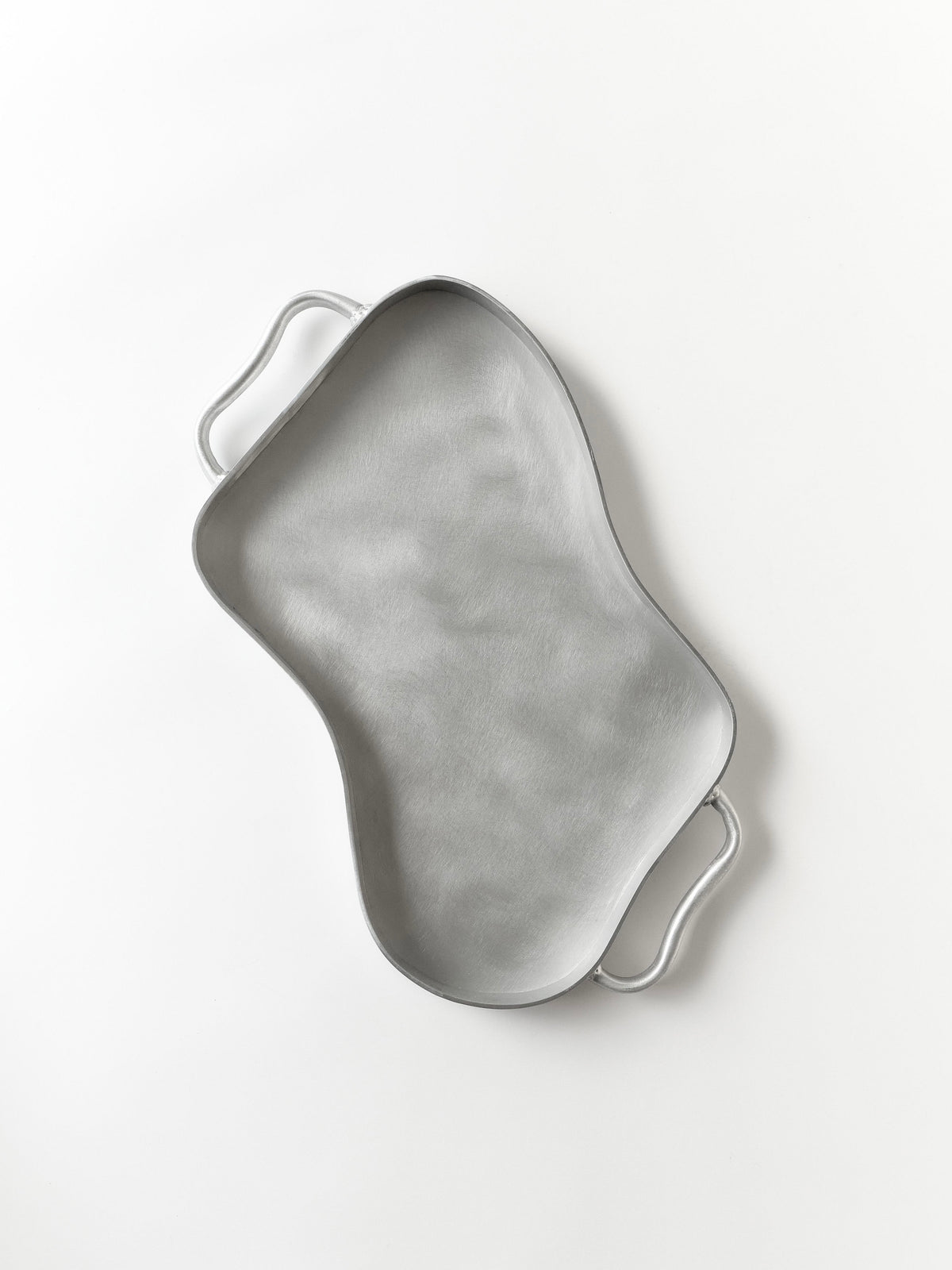 The Six Dots Design Serving Tray, handmade with a metallic abstract wavy surface and two handles, crafted in a North London workshop, is elegantly displayed on a light gray background.