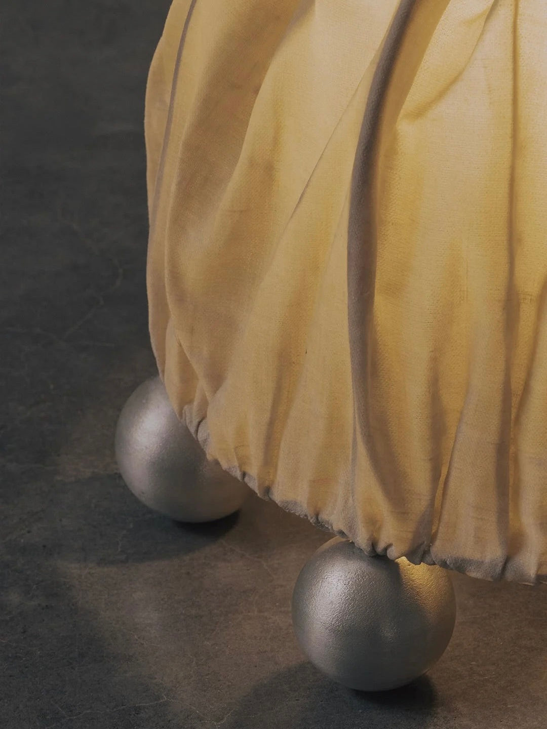 A close-up of the Kaytar "ALTER" Table Lamp, featuring a beeswax linen-covered sphere with a soft, pleated texture. It rests on a dark surface, supported by three metallic round balls that create a floating sculptural look.