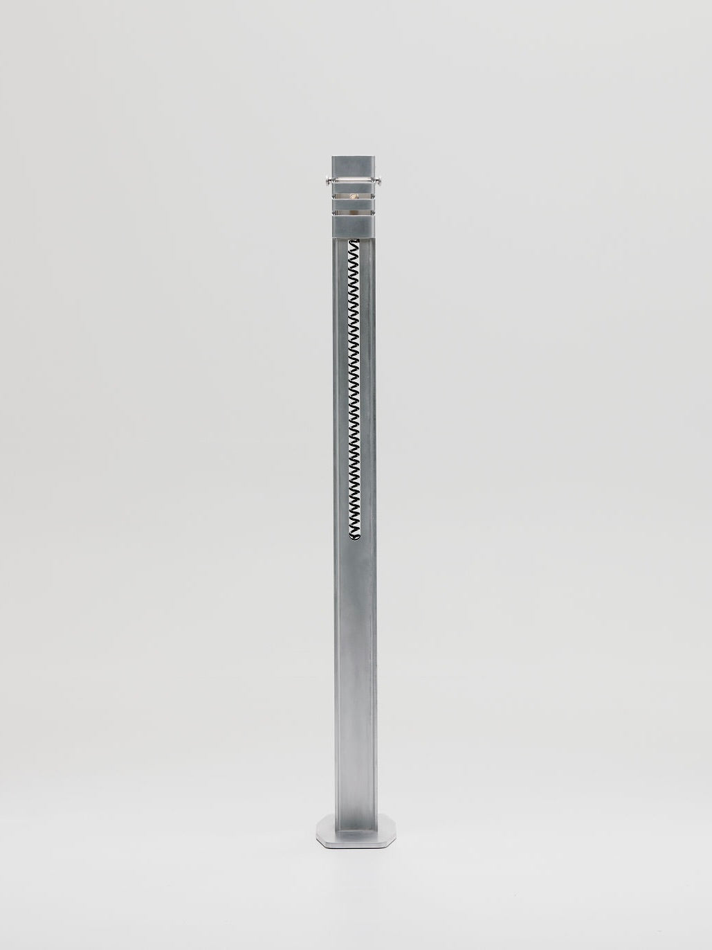 The Beam Floor Lamp by Marquel Williams features a tall, sleek metal post with a black and white chevron pattern, adding an artistic touch. It elegantly rises from a flat circular base against a plain white background.