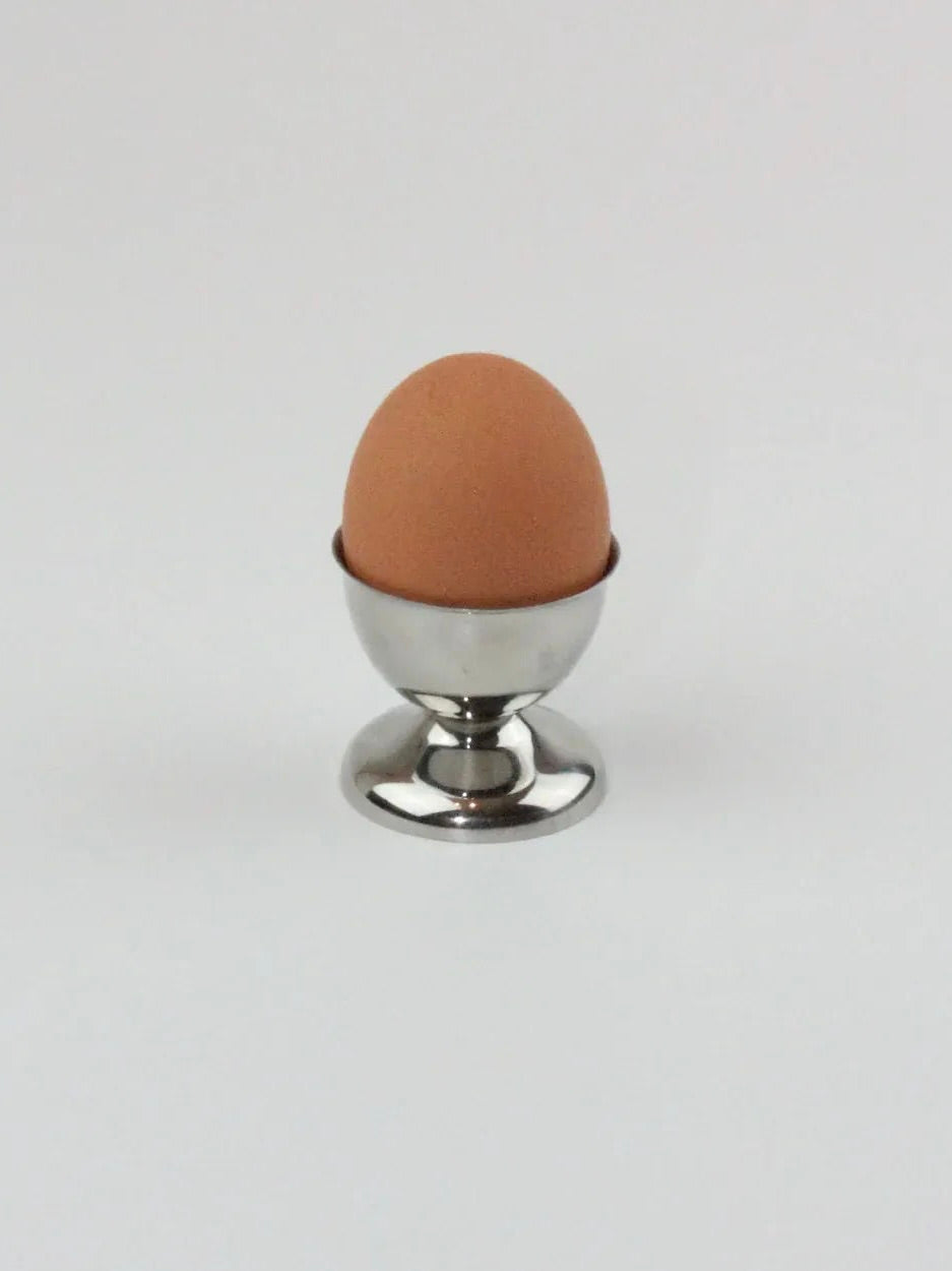 A brown egg stands upright in an elegant stainless steel egg cup from the Six Inox Egg Cups collection by Boga Avante Shop, exemplifying durability and strength against a plain white background.