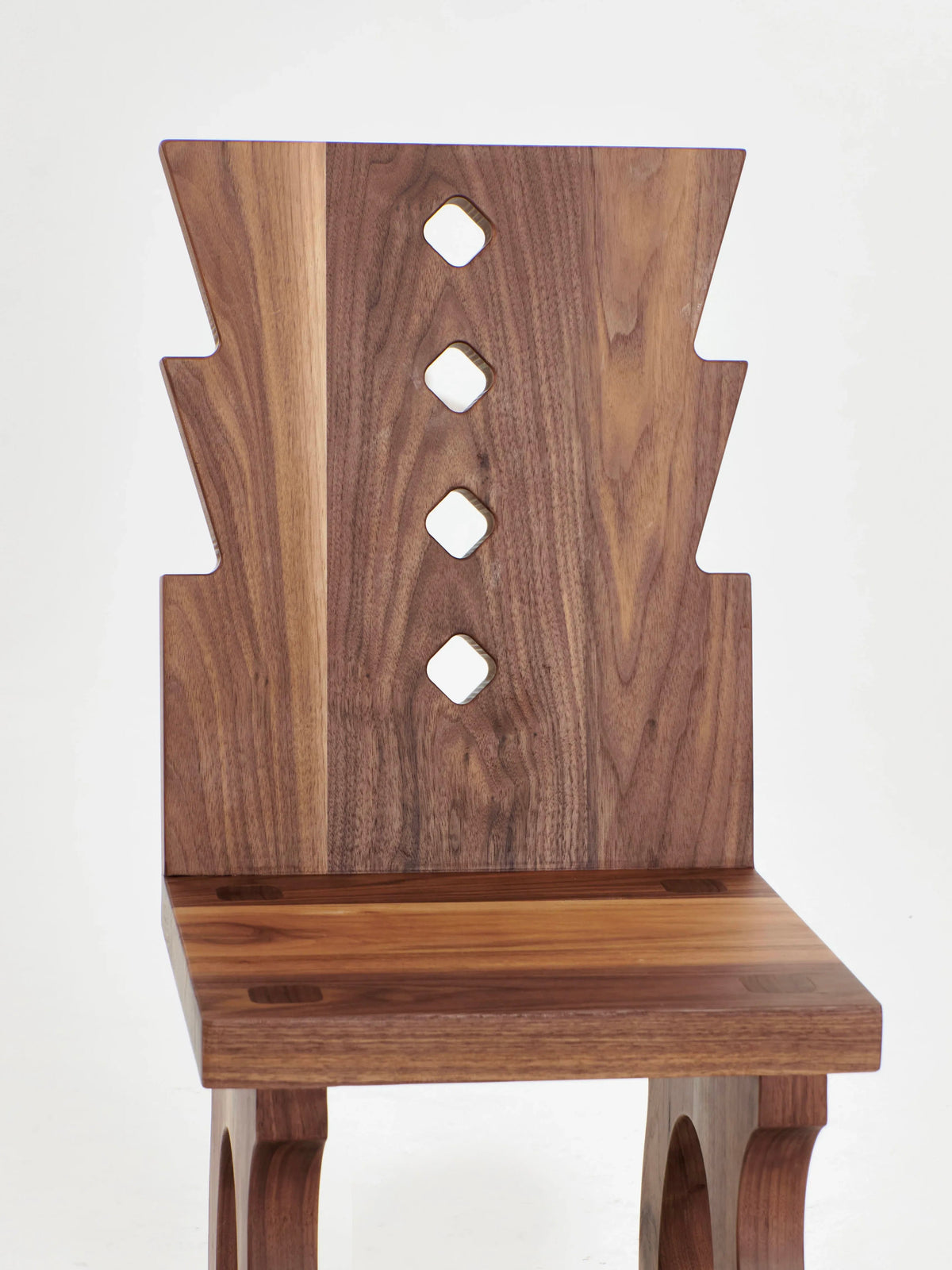 Introducing the Portugal Chair No 1 by Project 213A, a hand-carved walnut chair from Portugal. This elegant wooden chair showcases a distinctive backrest with four vertically aligned diamond-shaped cutouts in the center, complemented by angular, geometric patterns on its edges. Both the seat and legs are expertly crafted from rich-hued wood.
