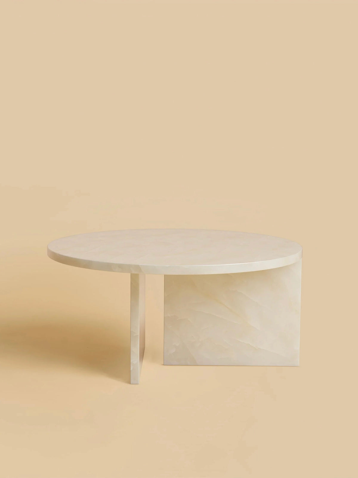The "Hashi" Coffee Table by Lebanto showcases a minimalist, circular design with an asymmetric base in light cream. Its solid beige background complements the smooth, polished surface and geometric lines, exuding contemporary elegance.