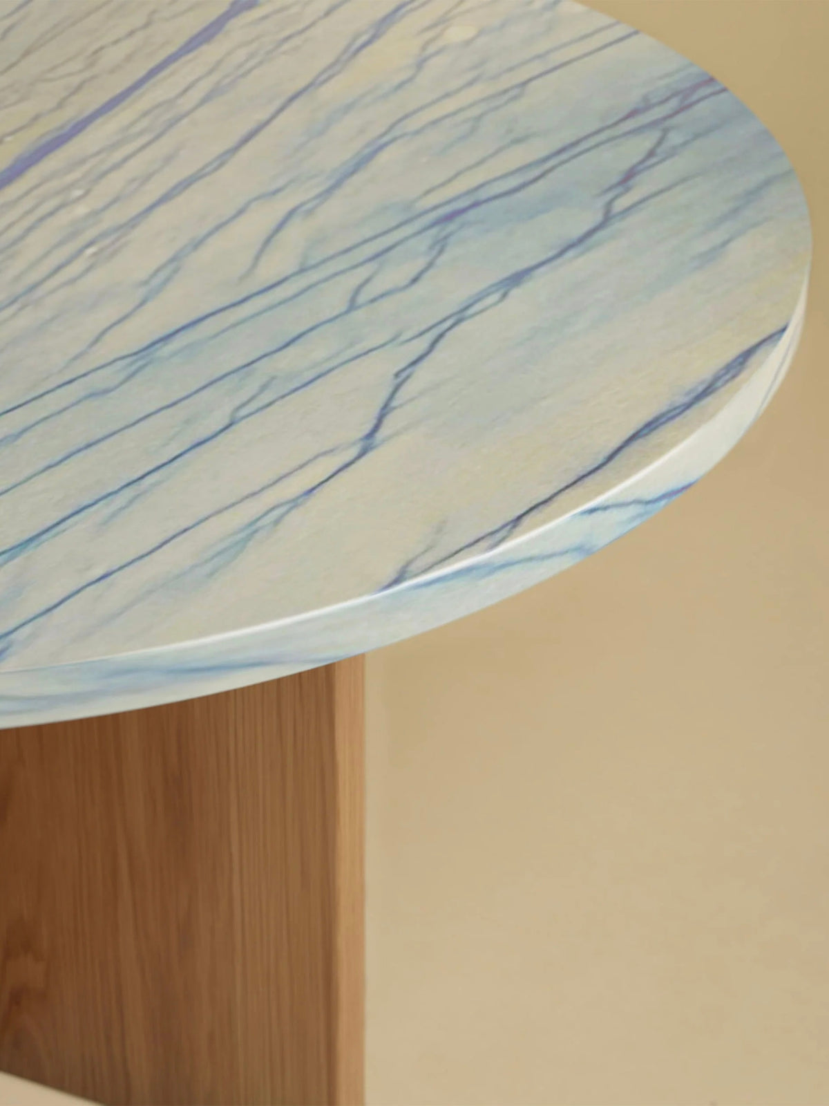 The Lebanto "Tinian" Coffee Table showcases a circular tabletop with a light blue, marble-like pattern featuring delicate veins, supported by an oak wood base, highlighting artisan quality against a neutral background.