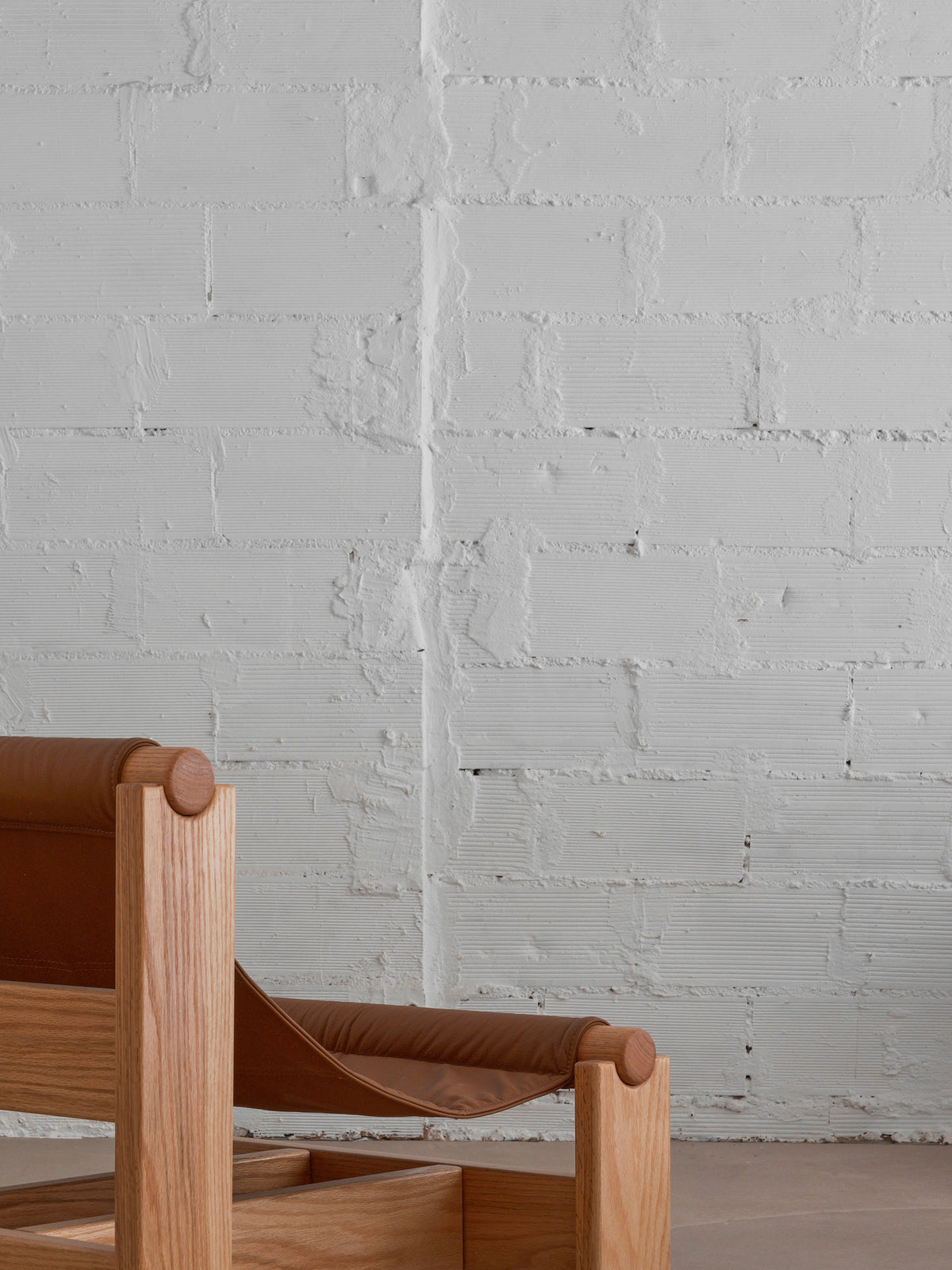 Minimalist scene featuring the corner of malva's "Lounge Up" Lounge Chair with brown leather upholstery, set against a textured white brick wall for a simple, modern, and elegant aesthetic.
