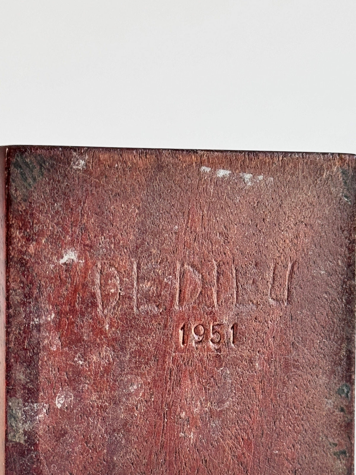 A close-up of a worn, brown leather surface with the text "Figuresdesign" and the year "1951" embossed into it. The leather shows signs of aging, with scratches and faded areas, reminiscent of an antique work named Exotic Wood Sculpture by Pierre Dedieu.