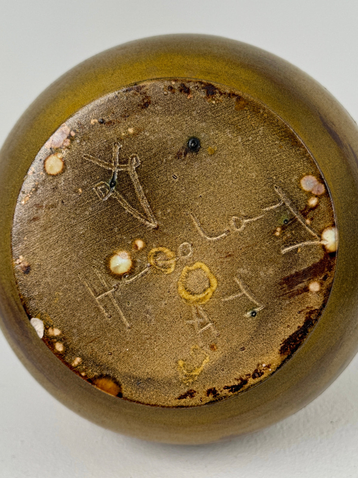 A close-up of the bottom of the Figuresdesign Ceramic Vase by the potters of Accolay reveals an inscription with symbols and letters. The surface, detailed with incised geometrical designs and irregular brown and white speckles, provides a rustic, textured appearance.