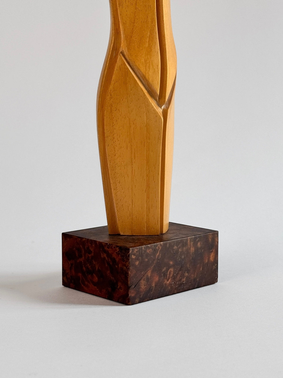 Crafted by Pierre Dedieu, this light wood sculpture from Figuresdesign showcases an elegant abstract design. It is beautifully presented on a dark, textured square base set against a light gray background.
