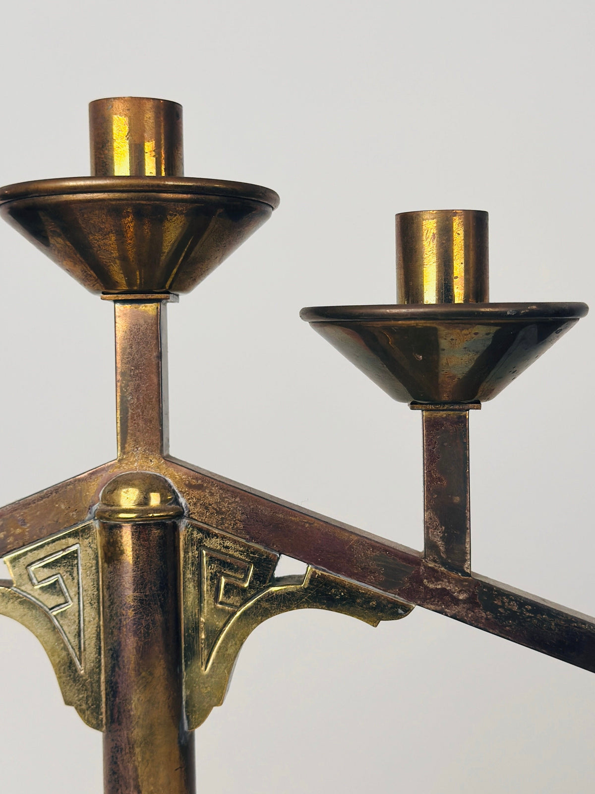 A close-up of a Figuresdesign Modernist Candleholder reveals its two candle sockets placed at different heights. The metal, in good condition, features a slightly tarnished, aged appearance with a nice patina. The design includes some ornamental detailing, set against a plain, light gray background.