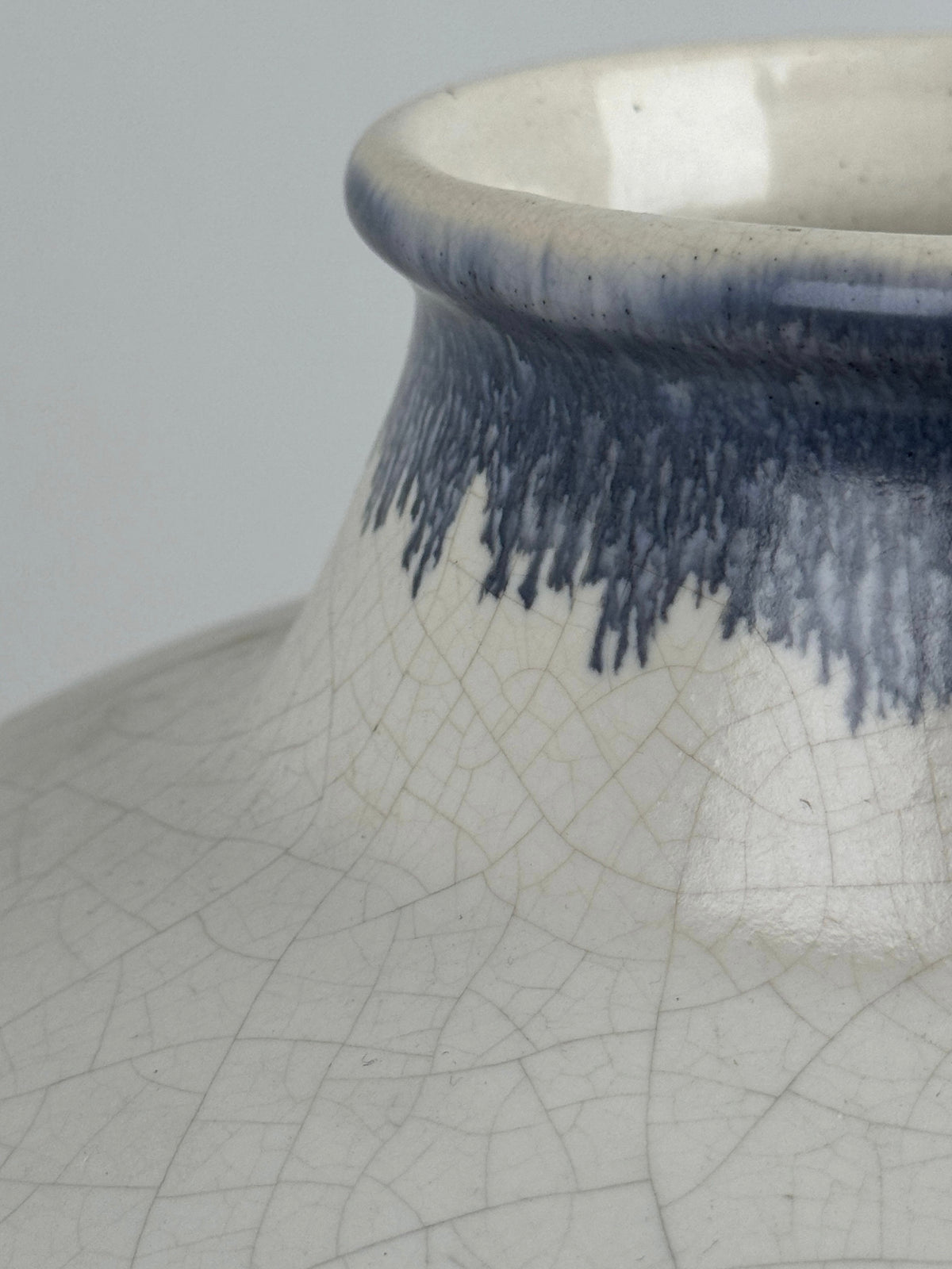 Close-up of a Figuresdesign Large ceramic vase by Ateliers Primavera featuring a wide neck. The vase is glazed in off-white with an elegant deep blue drip pattern near the top. Its crackled texture and vintage aesthetics are beautifully highlighted by craftsmanship reminiscent of polychrome enamel designs.