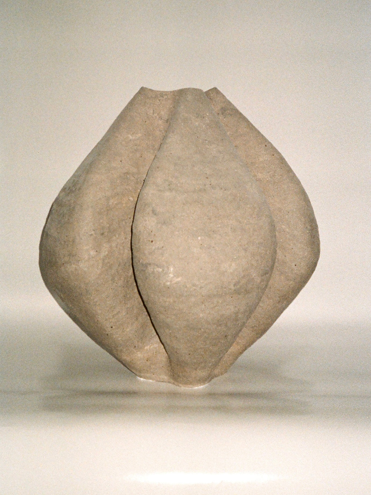 Growing Vase n.4 by Aiste Bagdonaite is a smooth, light-gray abstract sculpture with four curved, petal-like segments converging at the center, reminiscent of a handbuilt vase and set against a plain white background.