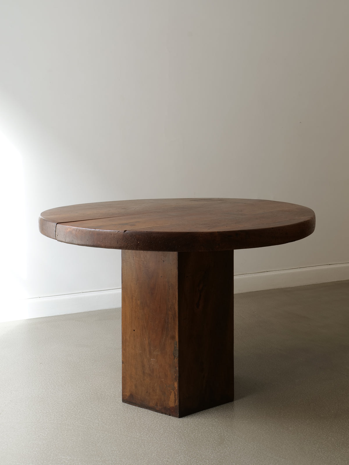 The Collection apart Midcentury Hexagonal Wood Dining Table, featuring a thick hexagonal top and sturdy rectangular base, stands on a light floor by an off-white wall, bathed in natural light from the left.