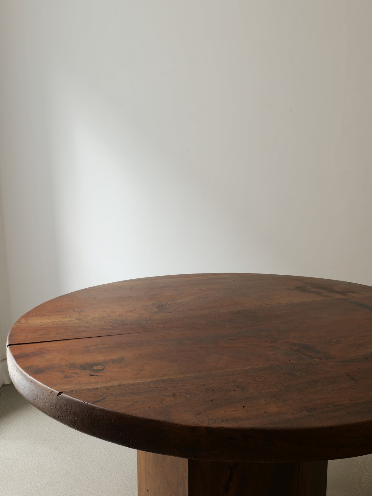 The Midcentury Hexagonal Wood Dining Table by Collection apart, with its dark, rustic finish, is featured in a minimally decorated room with light-colored walls and gentle natural lighting.