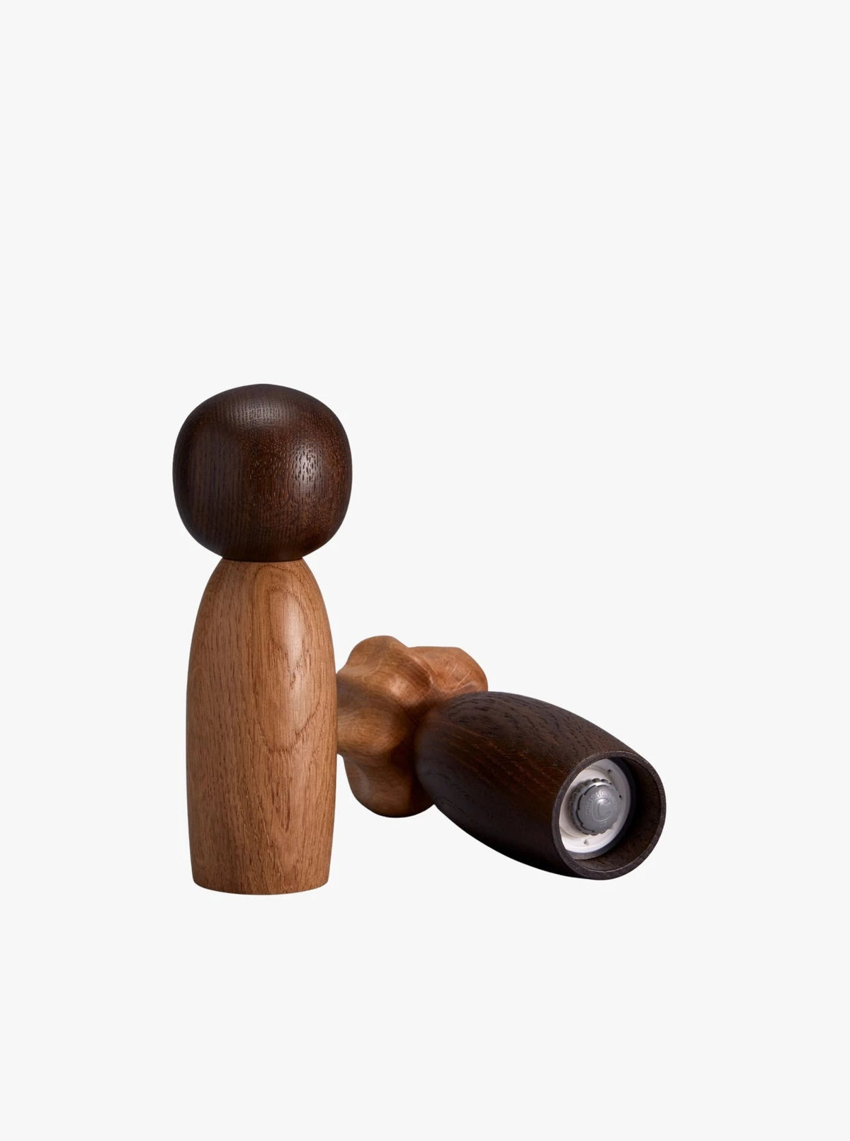 The Picanto Salt + Pepper Mills by LOBJET showcase a minimalist aesthetic, featuring one upright mill with a dark round top and light body, while the other lies horizontally with a hollow interior. Their simple, smooth designs stand out against a plain background.