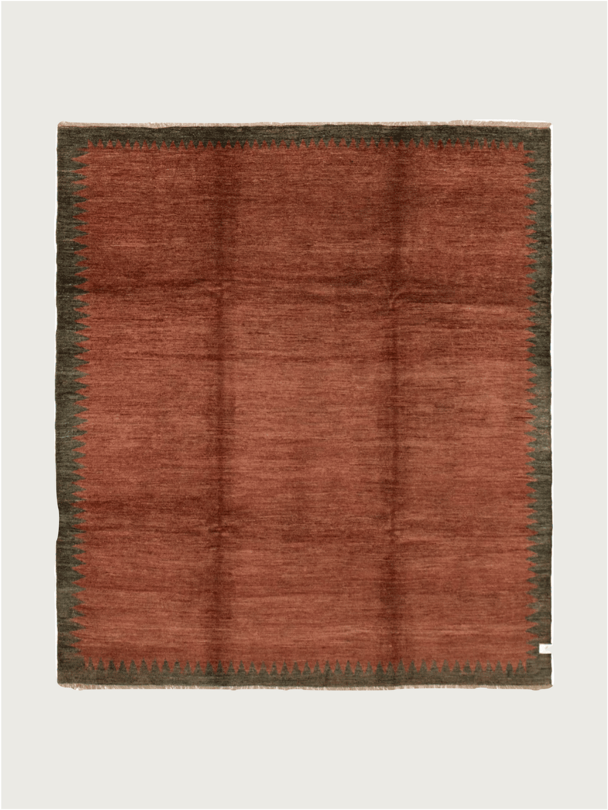 The Ziegler Rug in Carob by catalog:three is a square wool piece measuring 244 cm x 274 cm. It features a warm rust center with a dark green zigzag border, creating a hand-knotted, plush texture with subtle shading variances, set against a plain light background.