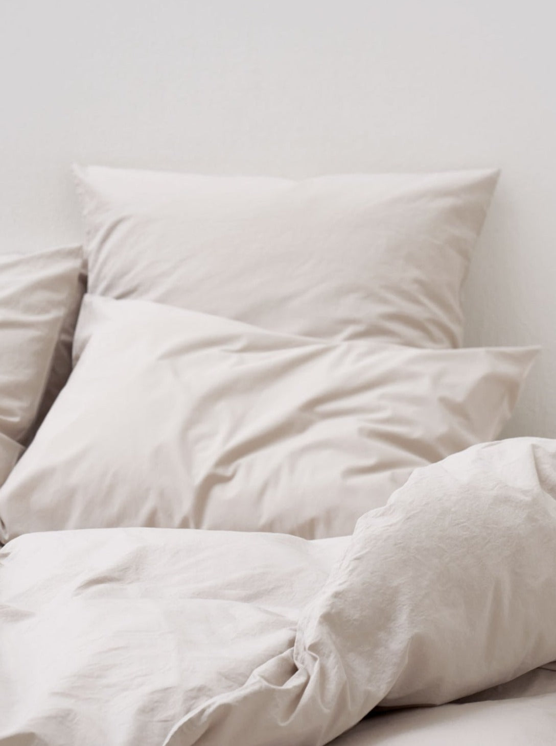 Two plush pillows on a bed, covered with MOST's Washed Cotton Percale Bed Set in Sand in a tranquil setting illuminated by soft natural light.