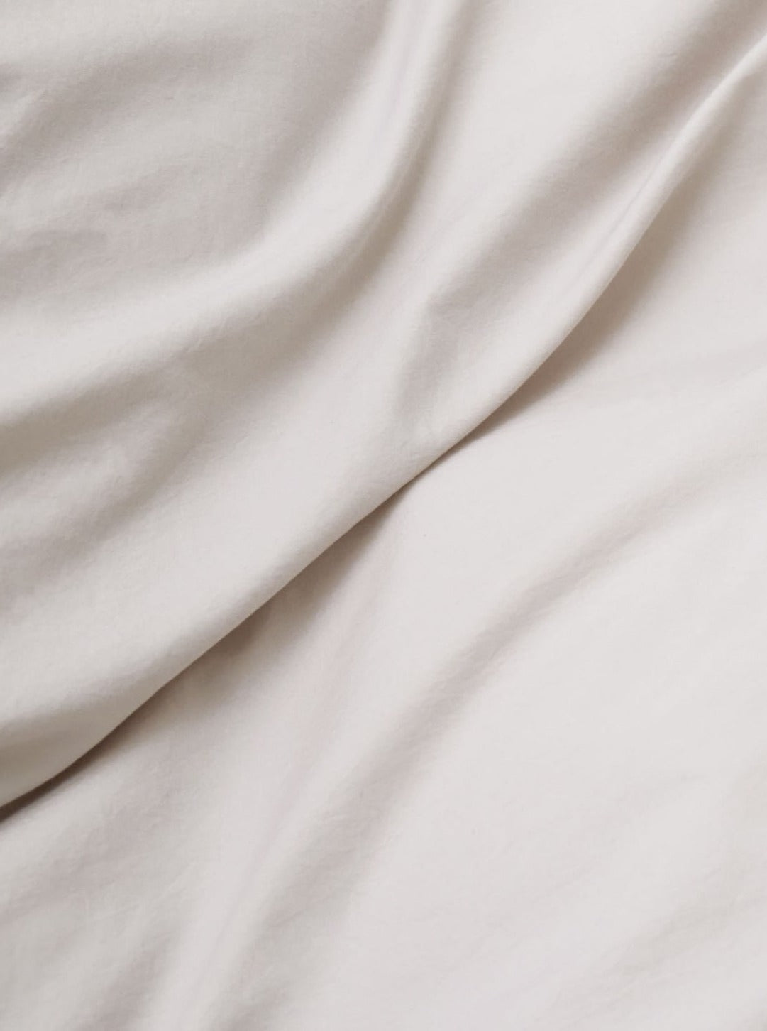 Close-up of a soft, white MOST Washed Cotton Percale Bed Set in Sand with smooth waves and subtle shadows highlighting its texture.