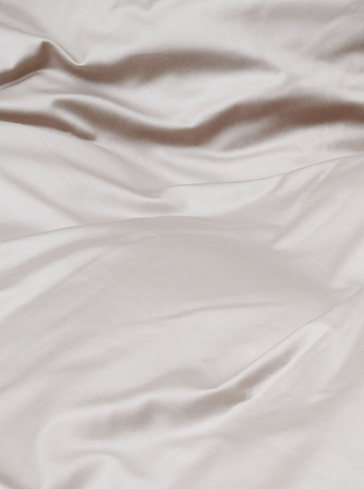 Close-up view of a smooth, cream-colored MOST Cotton Sateen Bed Set in Sand with natural folds and soft, flowing drapes.