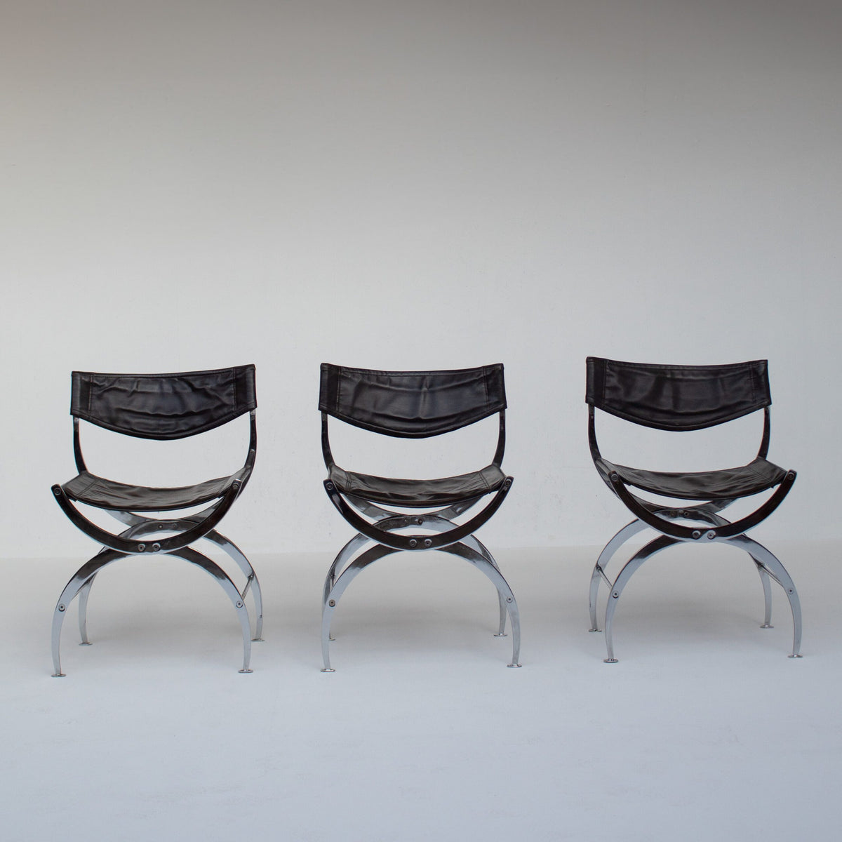 Set of 6 Italian Chrome Dining Chairs with Leather Seating — back view of three chairs in a minimalist setting