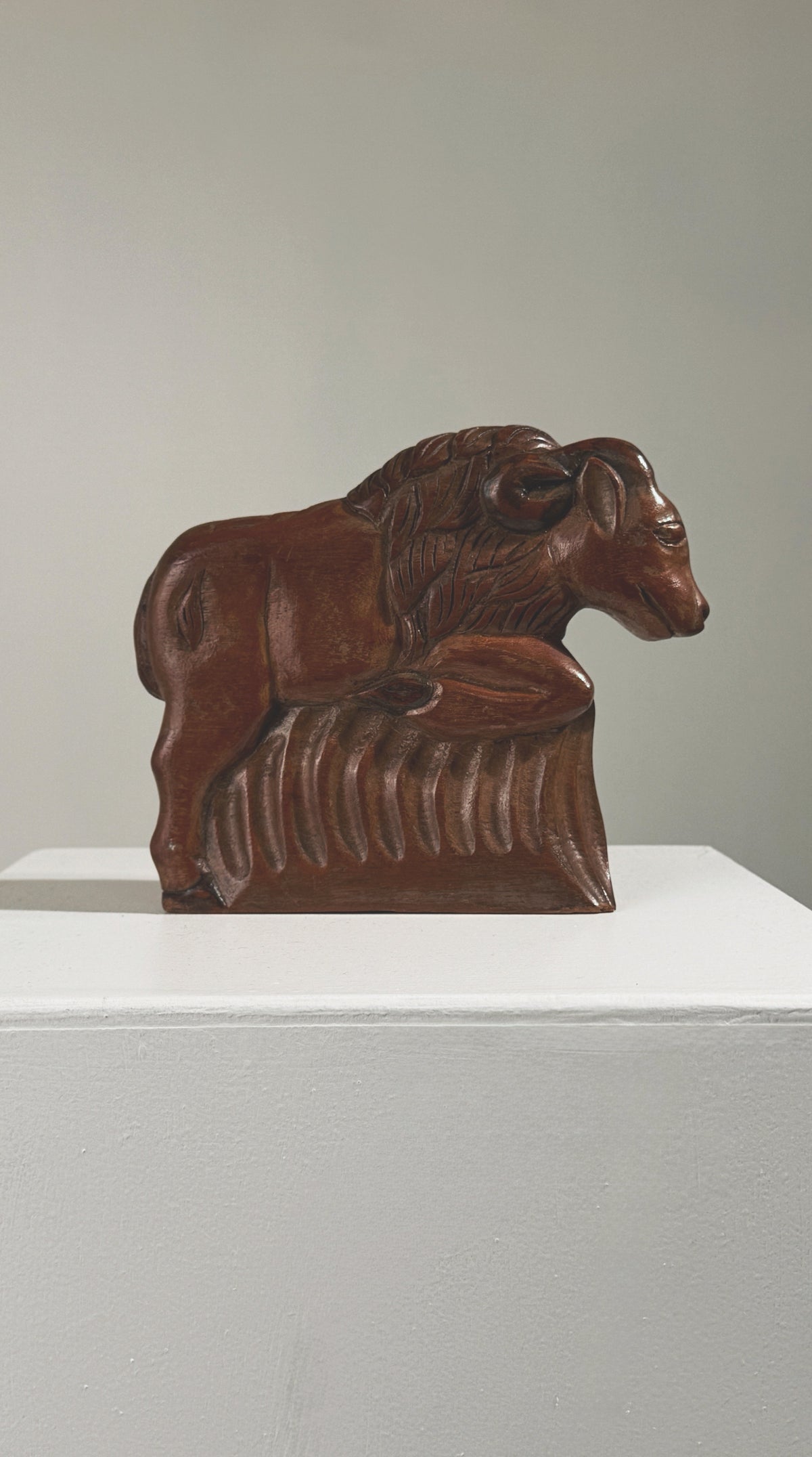 Antique carved wood ram sculpture resting on decorative base