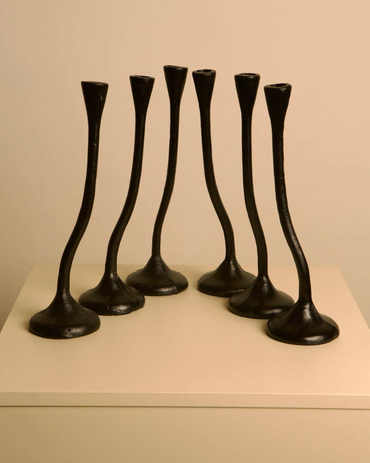 A set of 5 Treaptyque "Twisted" black cast aluminum candleholders from the 80s, featuring flared bases, is arranged on a light square surface against a plain beige background, showcasing sculptural design.