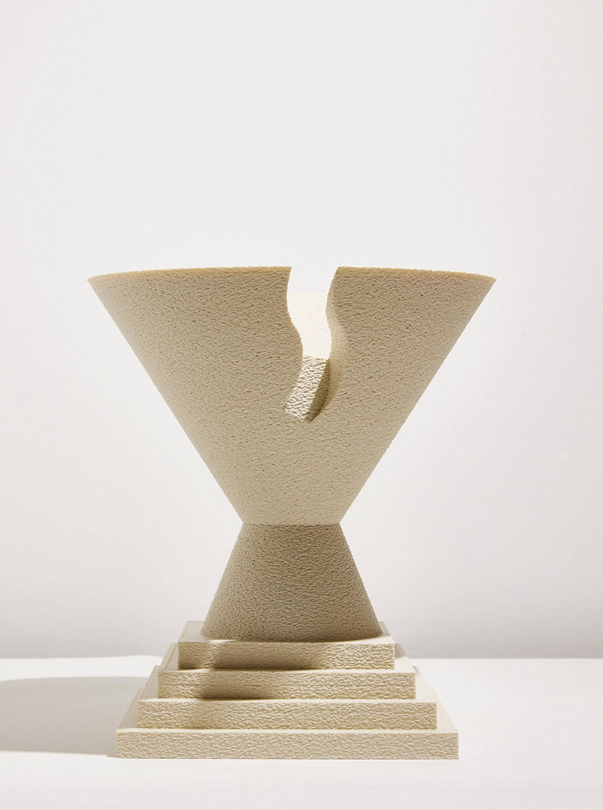 A textured, beige sculpture crafted using 3D printing technology, depicting a cracked trophy-like shape known as the Argot Studio Tyro Bowl, set on a matching square base, against a plain white background.