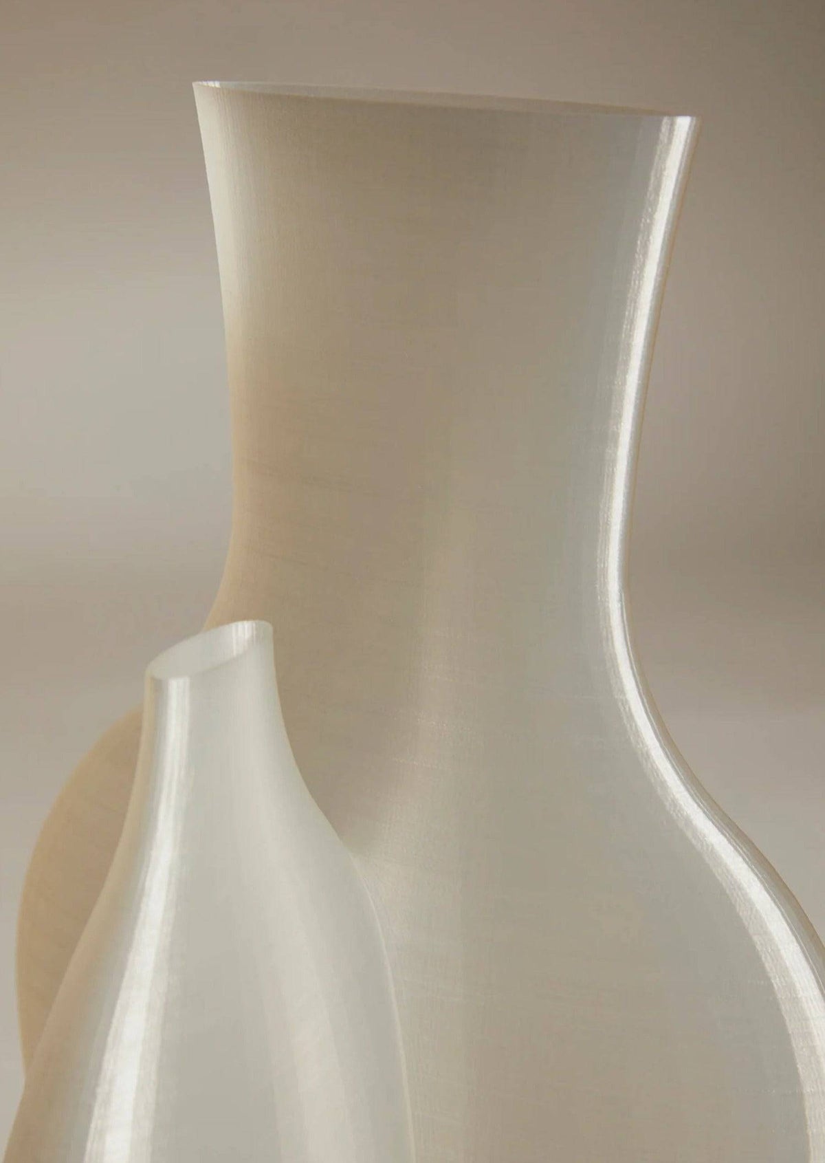 Against a neutral backdrop, two elegant Double Vessel - New Edition vases by Argot Studio showcase their sculptural beauty with smooth curves. The handcrafted larger vase stands behind, and the smaller one is in front, both reflecting light and embodying minimalist elegance.