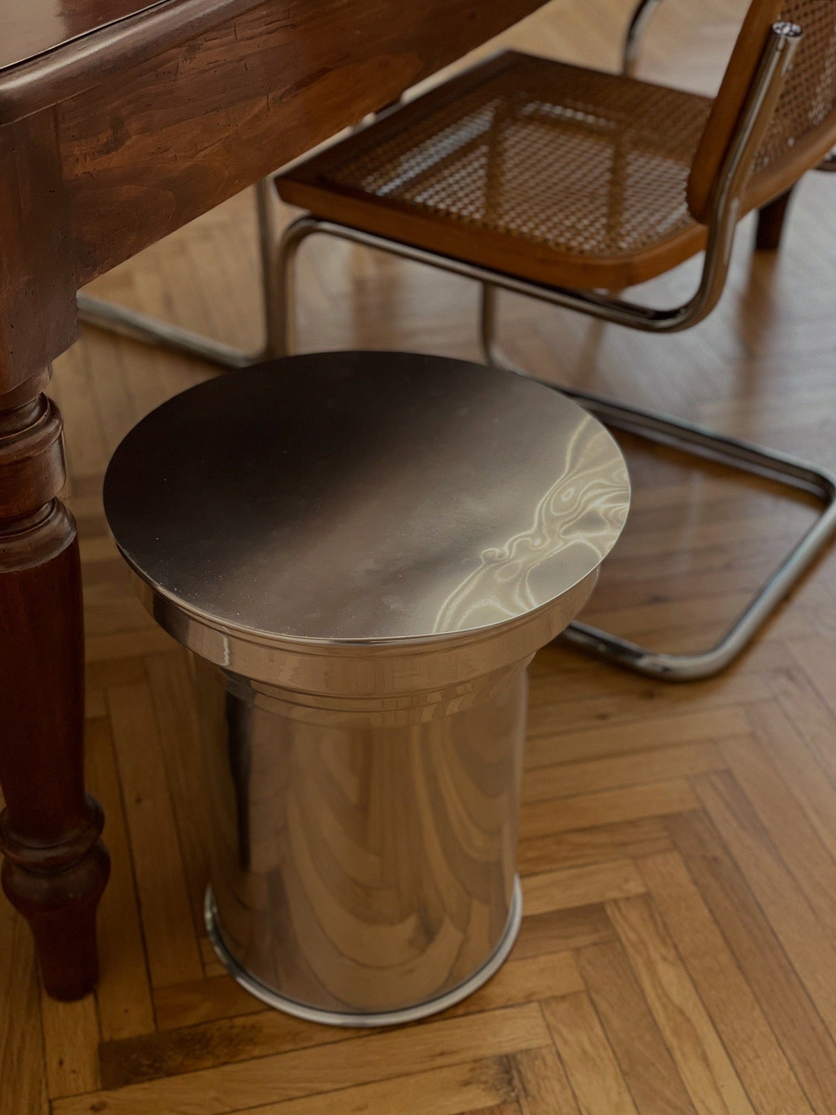 Art Deco Side Table - Mirror-Polished Metal Collection — angled view beside wooden dining table