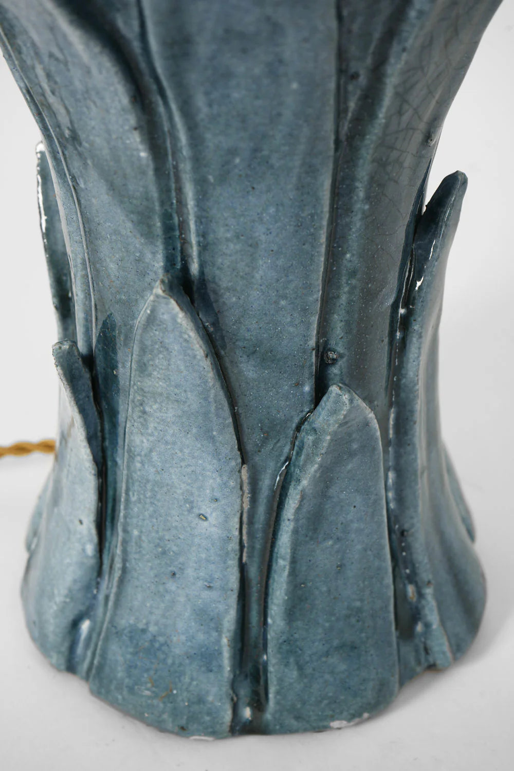 Close-up of the "Sintra" Blue Table Lamp by Barracuda Interiors, showing its blue-gray ceramic base with textured leaf-like ridges and a glossy finish. Made in Portugal; a yellow cord appears in the background.