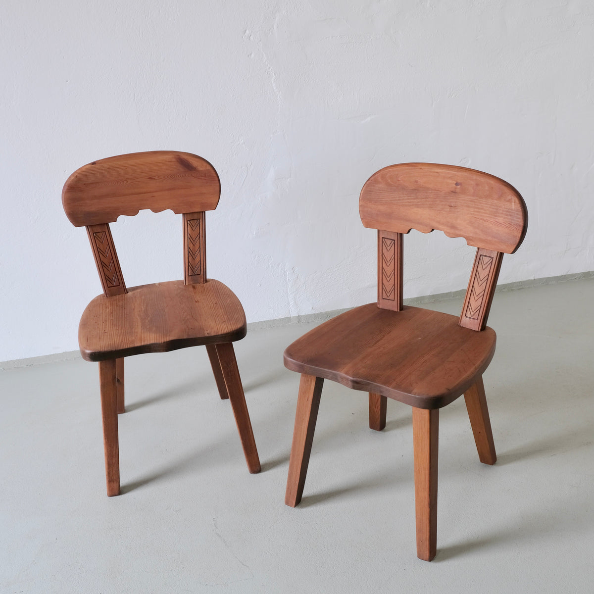 Two rustic carved pine chairs with decorative backrest details