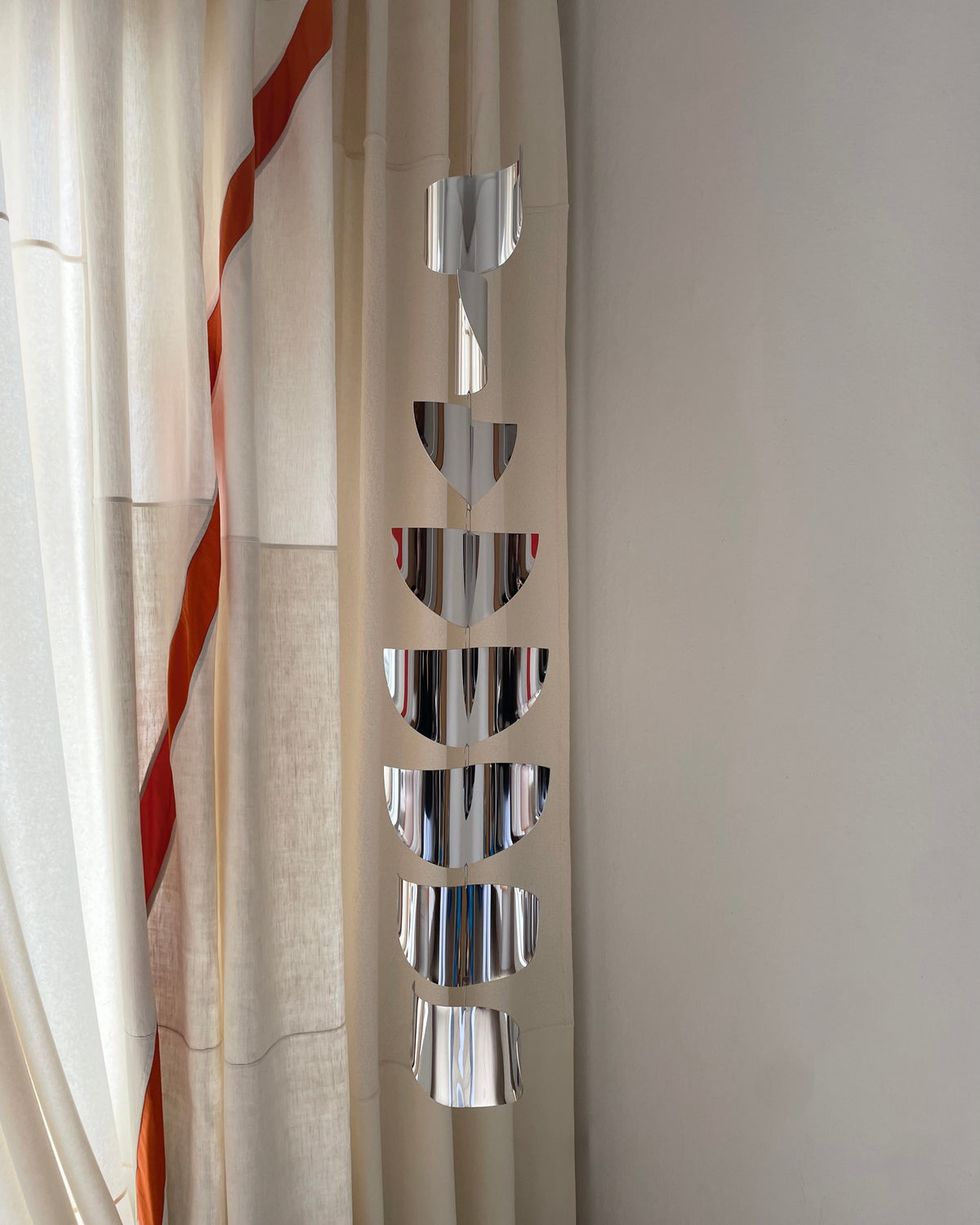 Chrome moon phase mirrors arranged vertically on beige curtain