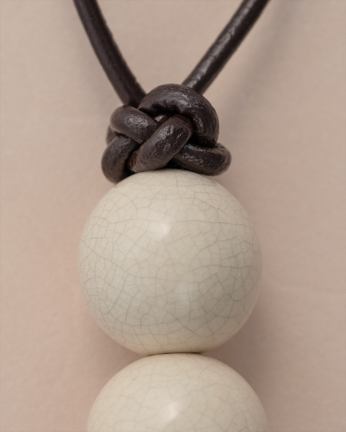 Close-up detail of white ceramic beads on dark leather cord tassel