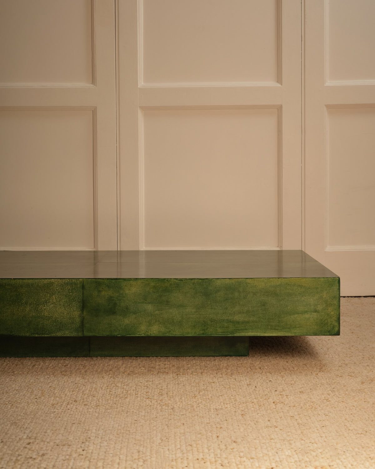 The Green parchment table by Galerie Vauvart, a minimalist Italian design, sits on a beige textured carpet against cream paneled walls.