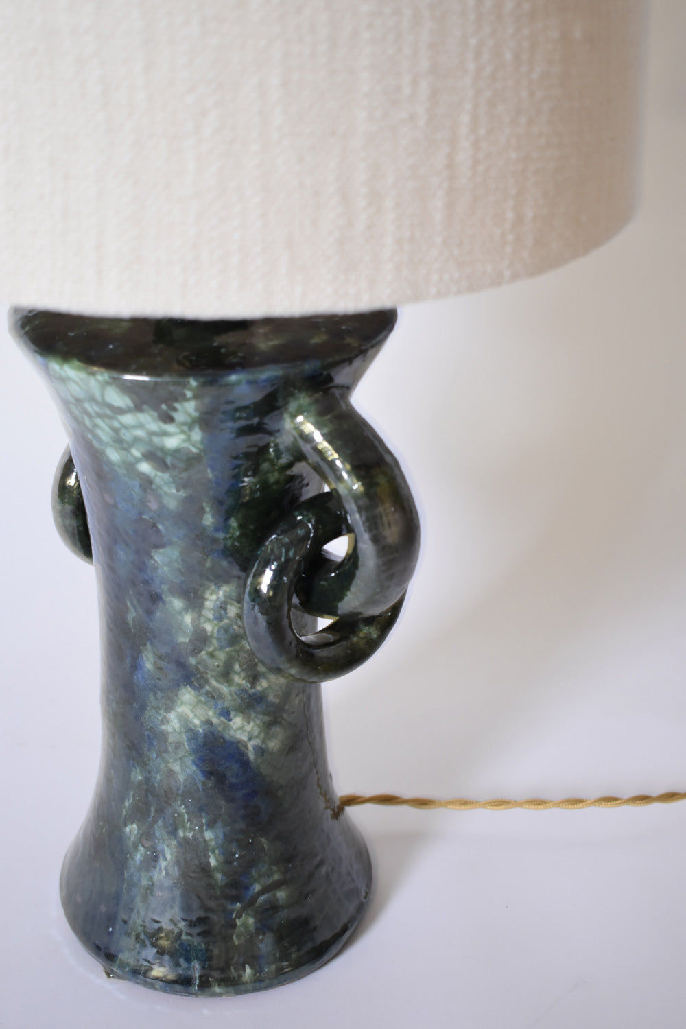 The "Kasaï" Blue & Green Ceramic Lamp by Barracuda Interiors features a glossy marbled base with curled handles, a textured off-white shade, and a yellow twisted cord visible on the white surface. Made in Portugal.