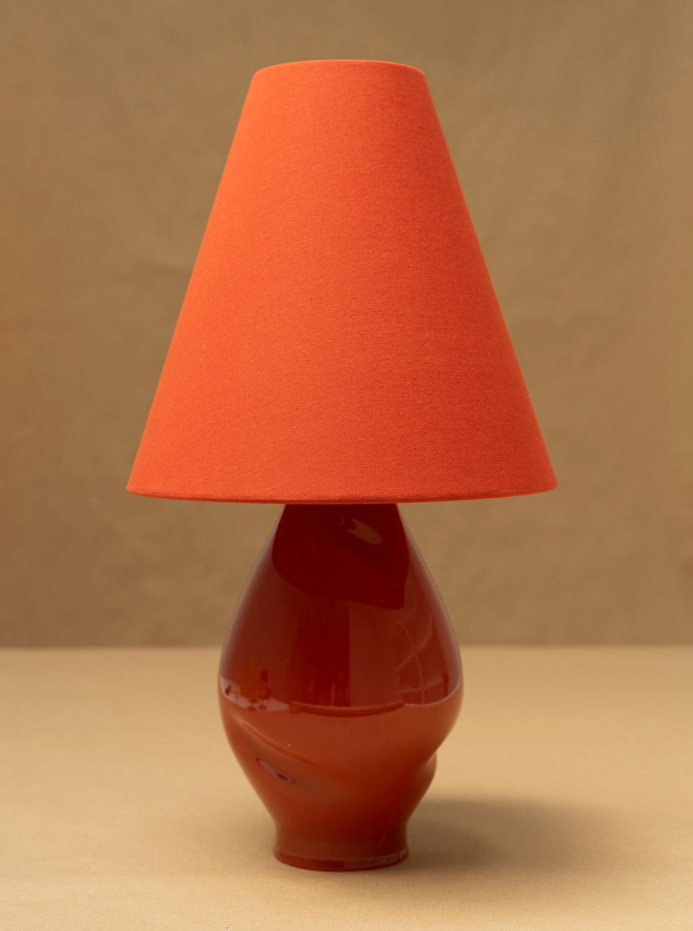 Dark red ceramic lamp base with orange conical shade, profile view