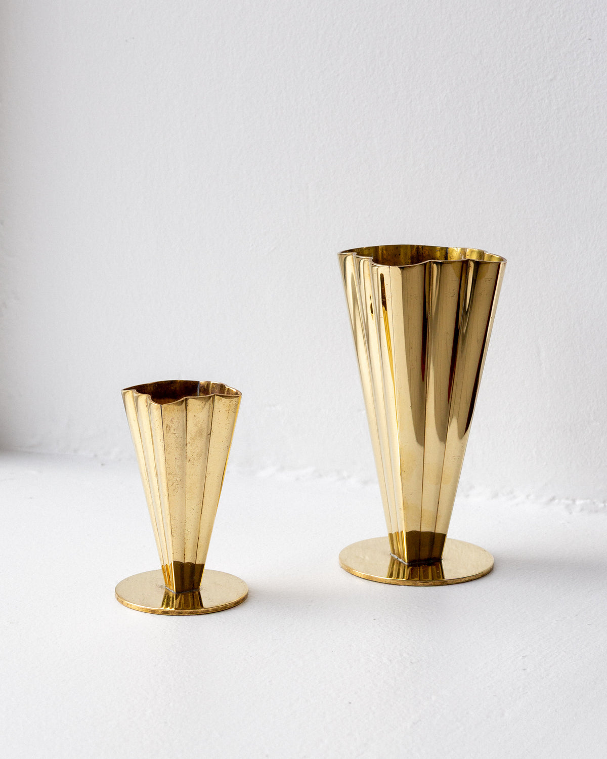 Two golden brass vases with fluted design on white background