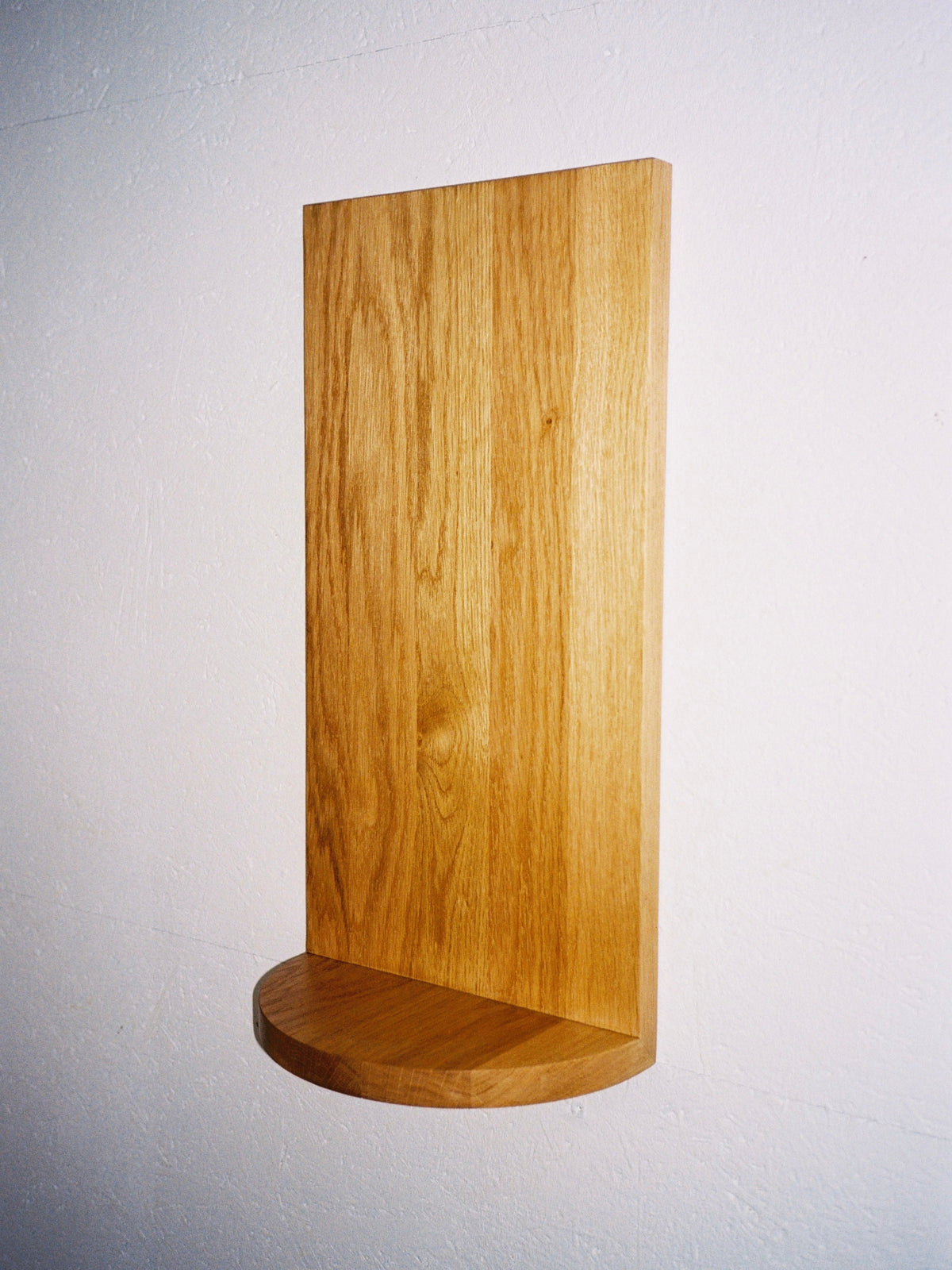The Megaron - Minimalist Shelf in Wood - Small by COSEINCORSO is a handcrafted solid oak shelf featuring a rectangular back panel and a small, semi-circular base, elegantly mounted on a white wall.