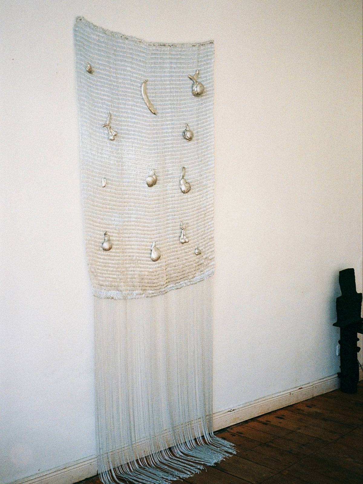 Handwoven textile wall sculpture with golden fruit ornaments and fringe