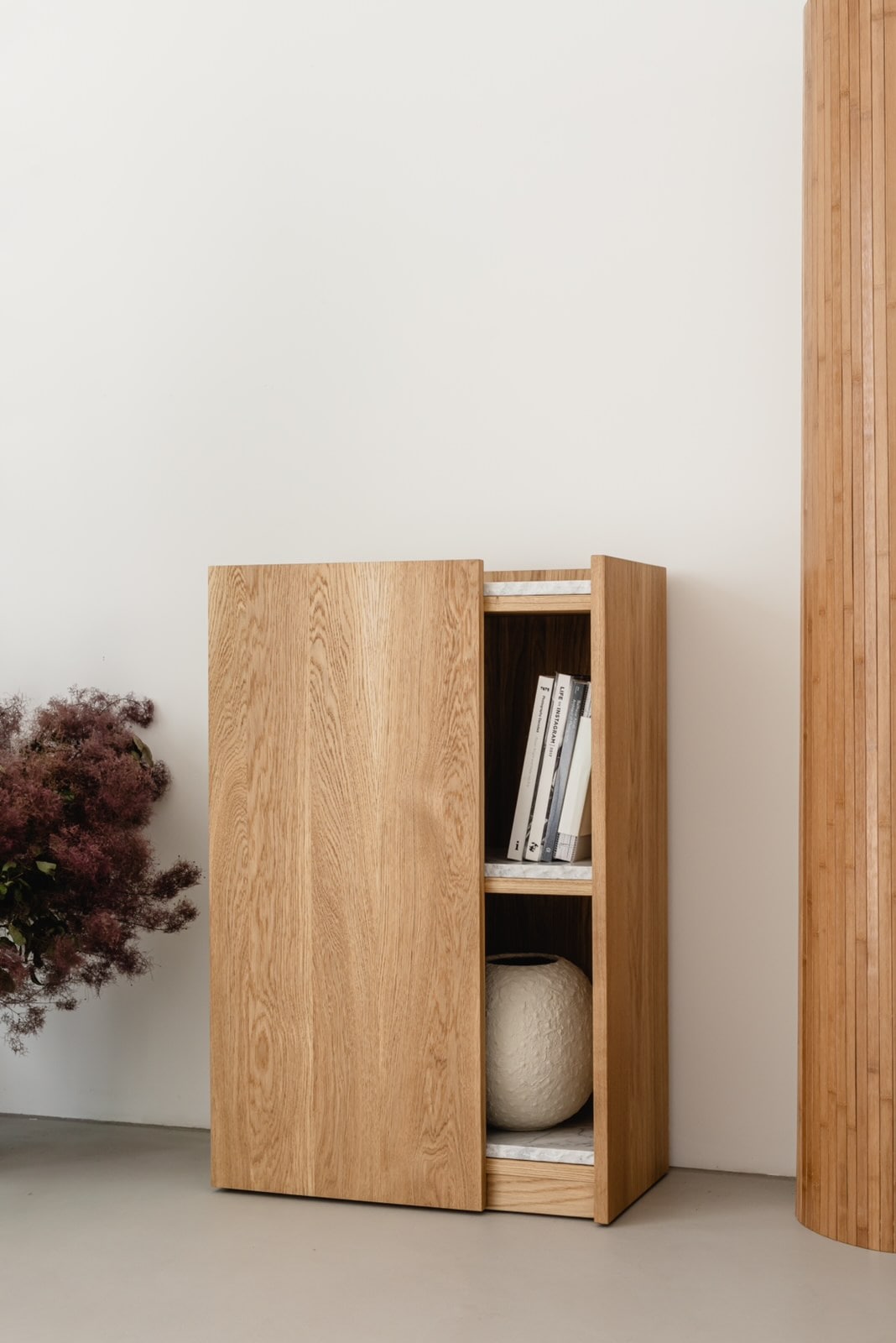 PAVO oak cabinet with sliding door revealing interior shelving and decorative objects