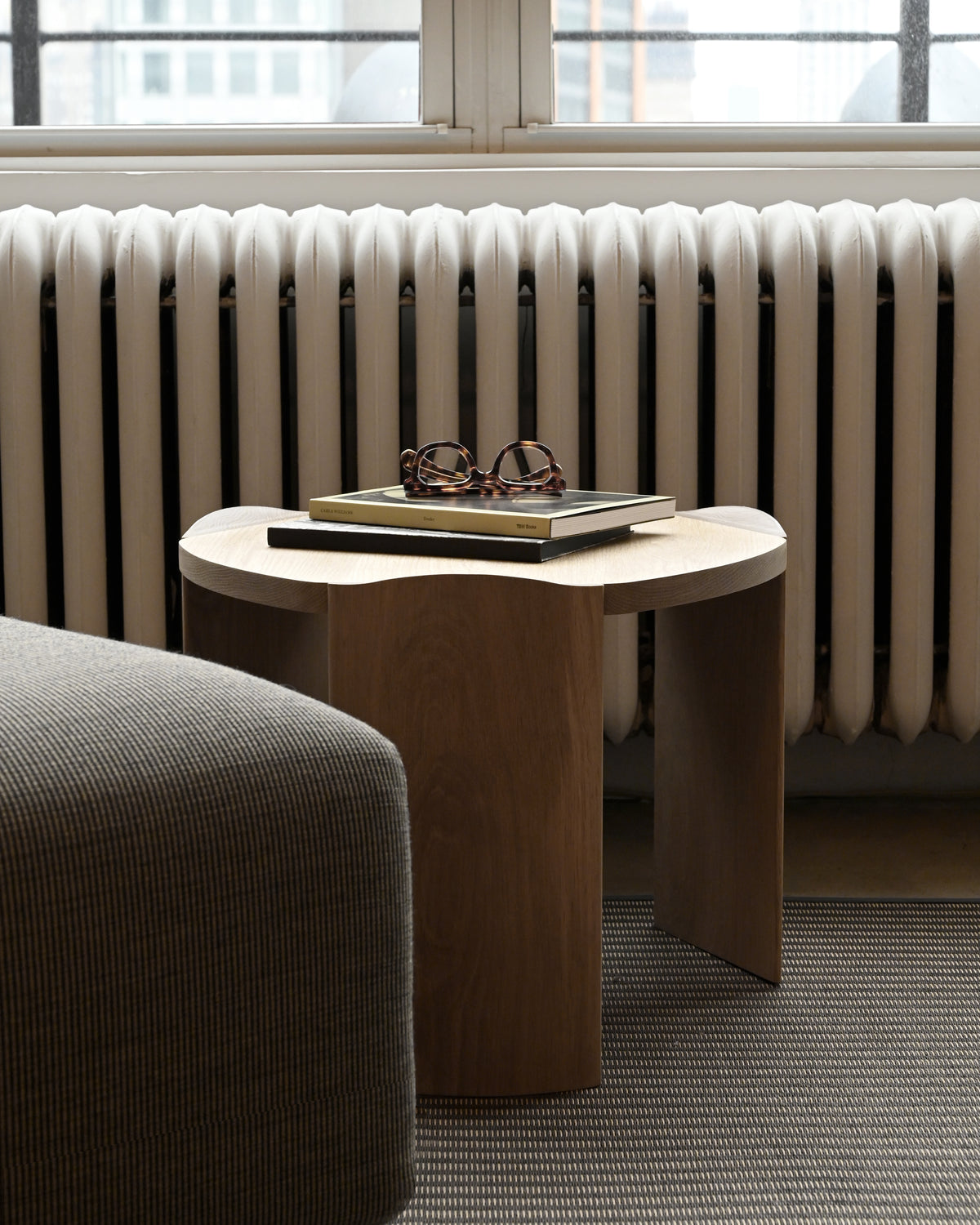 Round wooden occasional table with books and glasses styled by radiator