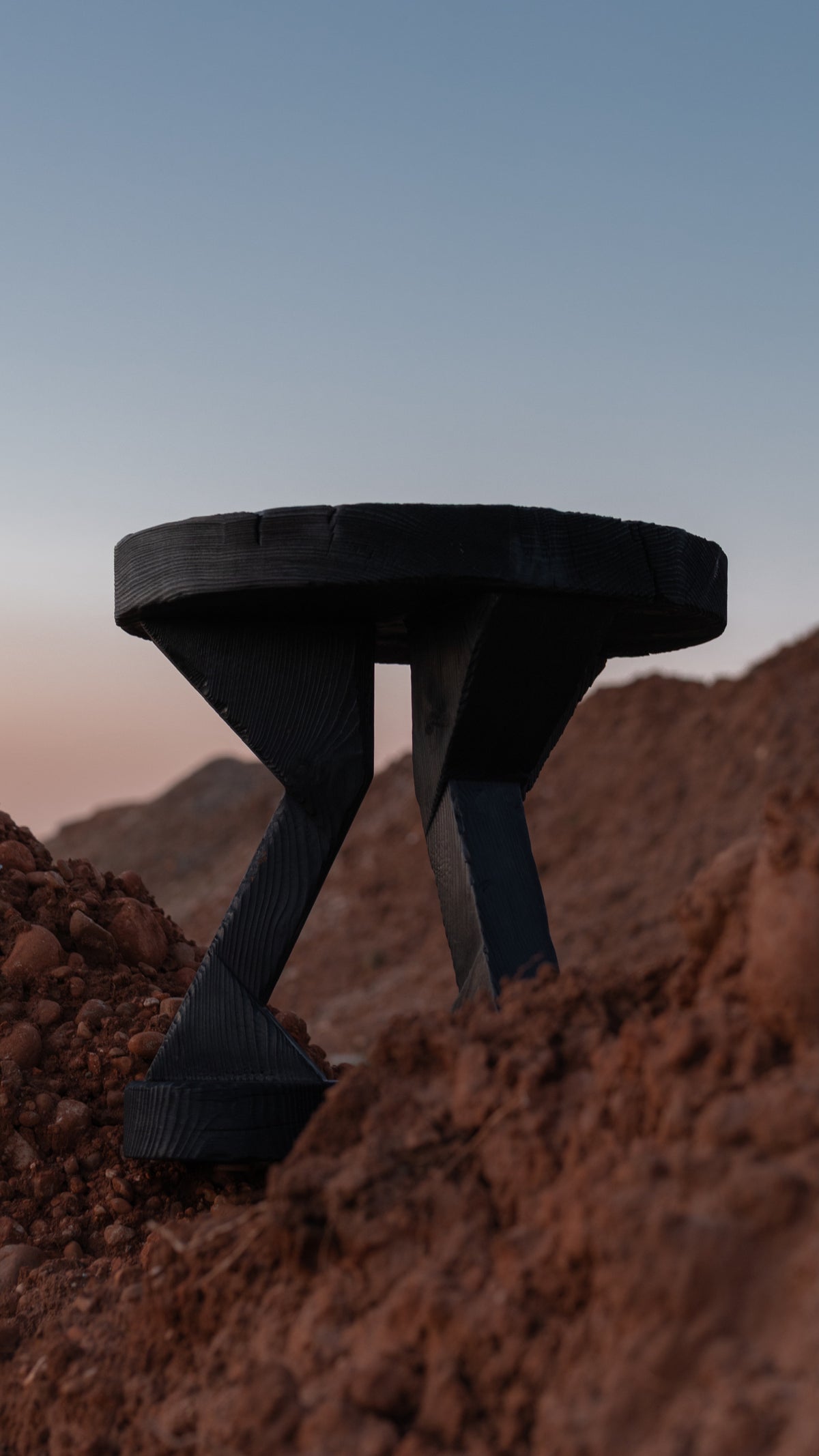 ABORA burnt wood end table with tripod legs in desert landscape