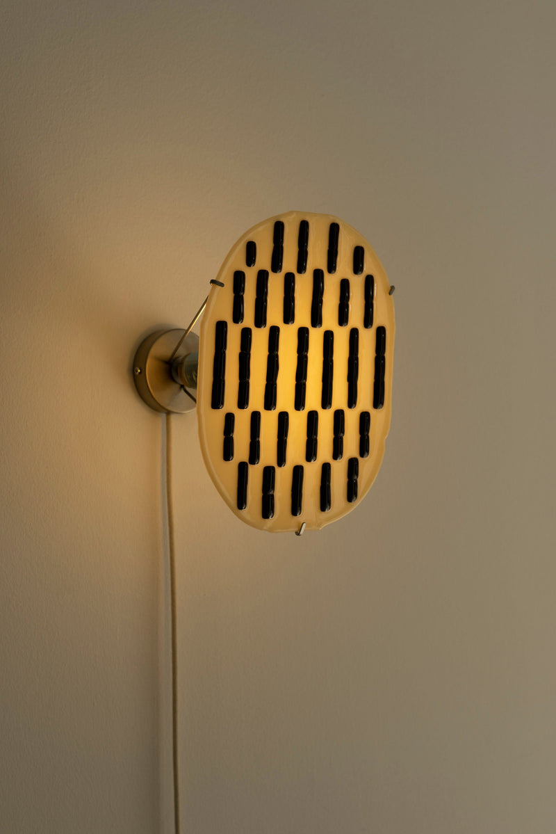 Beige glass wall sconce with black dash pattern, illuminated