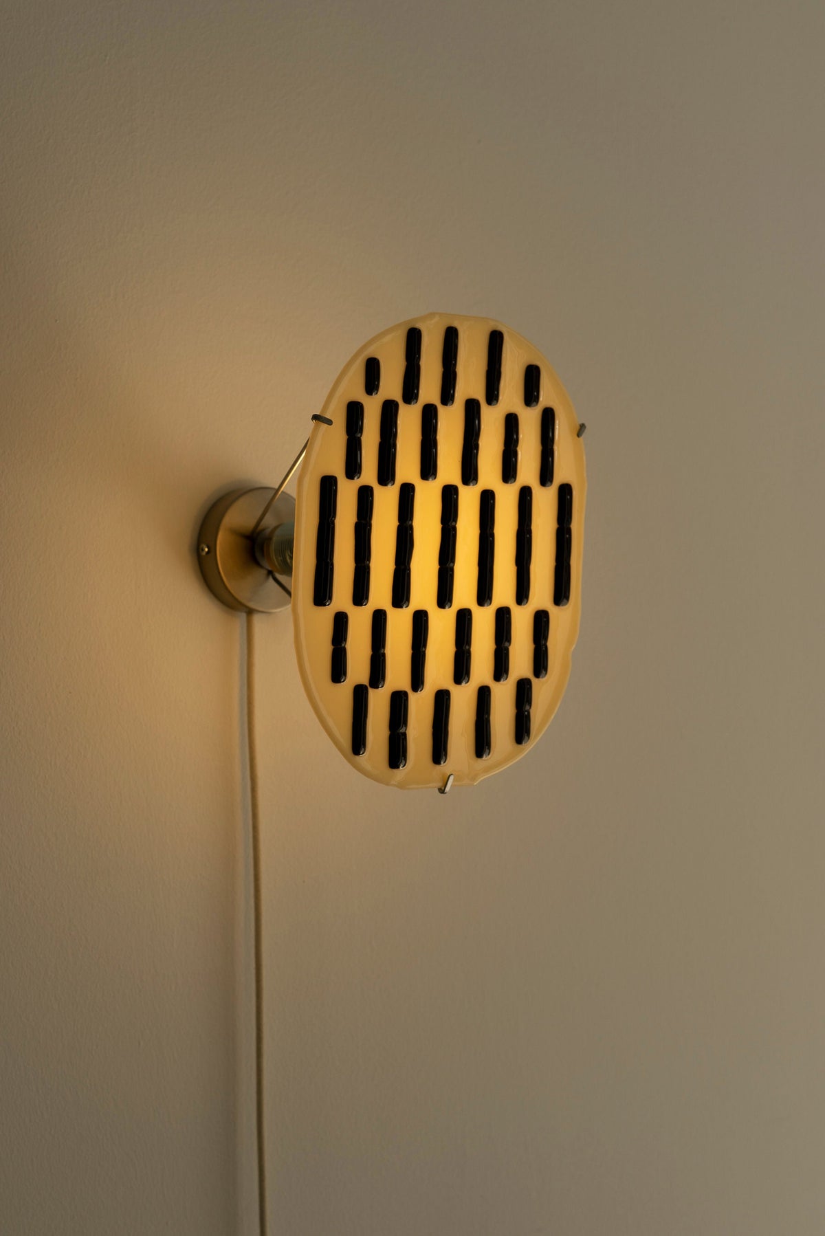 Beige glass wall sconce with black dash pattern, illuminated