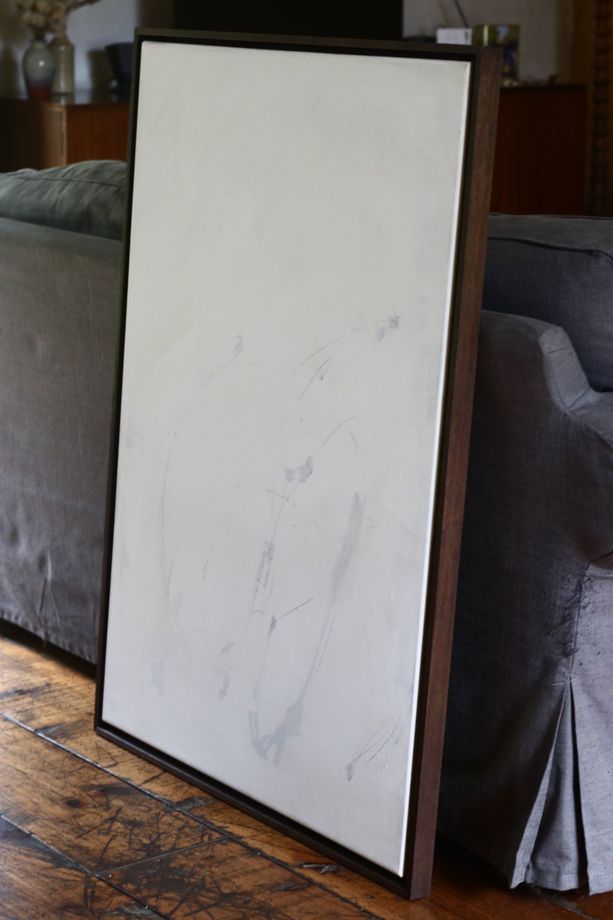 Mixed media abstract painting on linen in wooden frame leaning against sofa