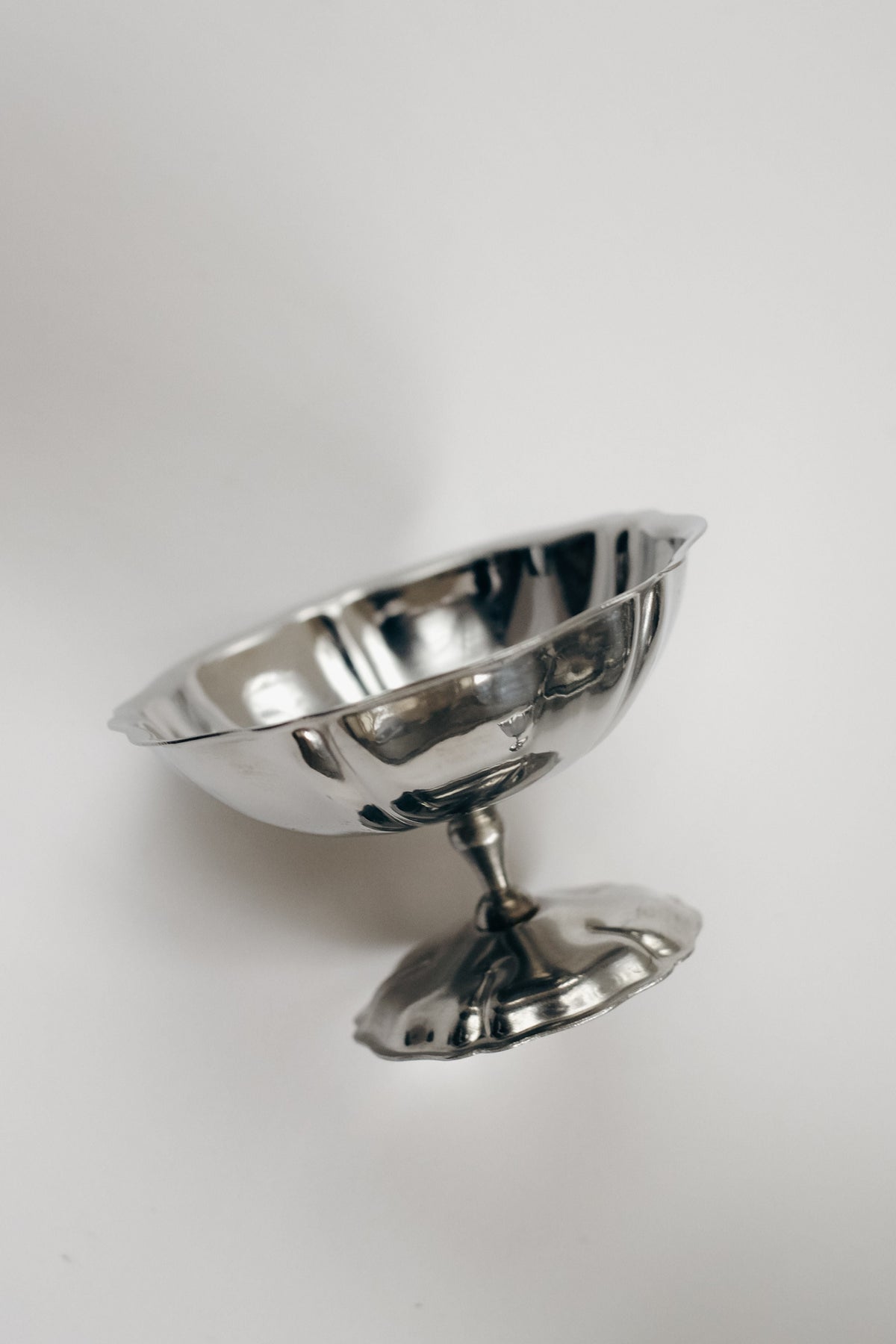 A reflective, empty vintage stainless steel ice coupe from the septembre studios Set of Six is shown on its side against a plain white background.
