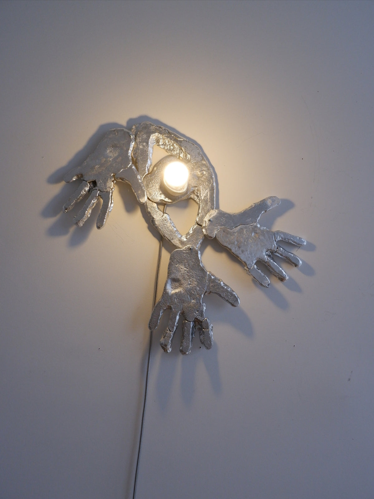 Sculptural wall lamp with bronze hands and illuminated center detail