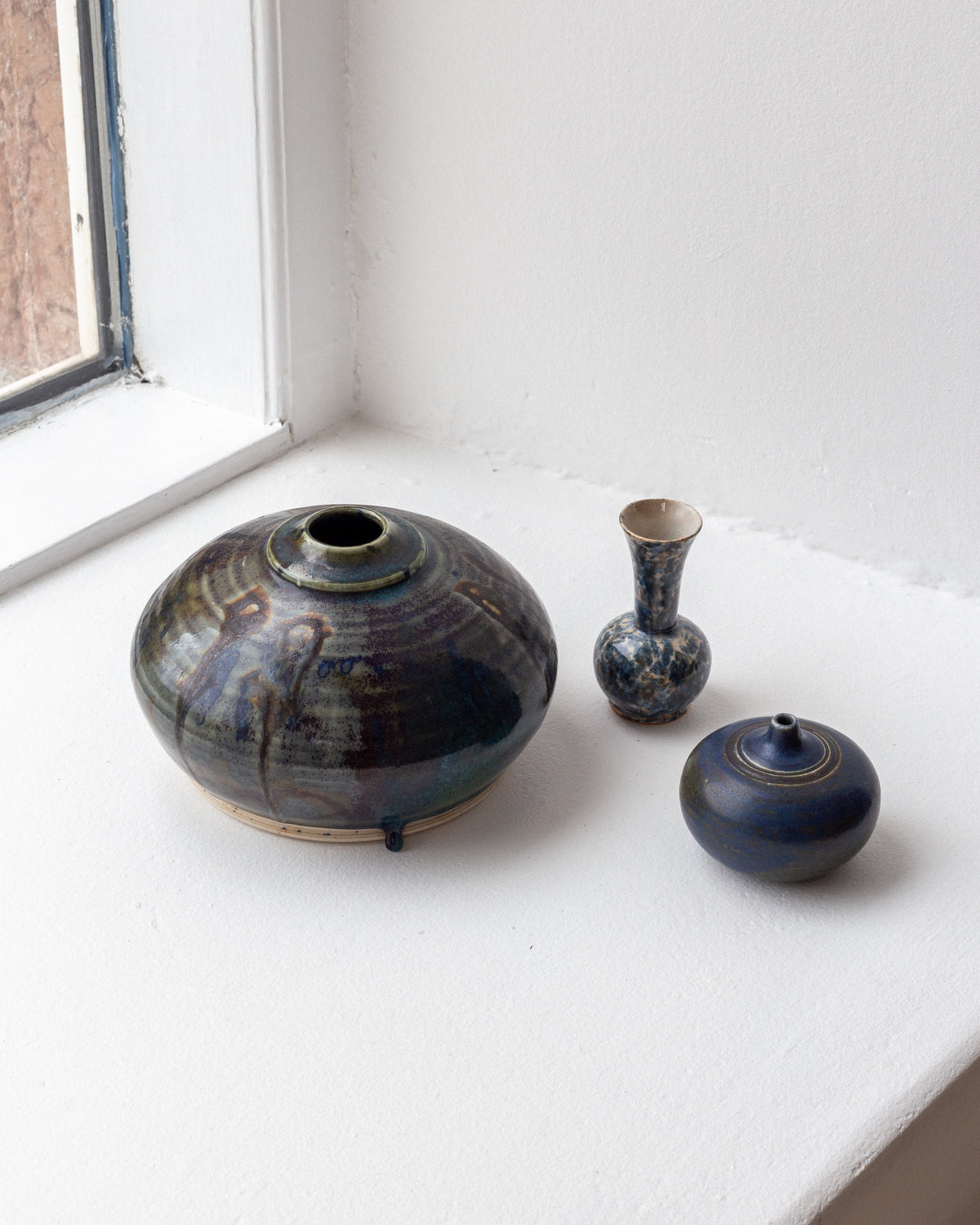 Studio pottery vases with drip glaze on white windowsill