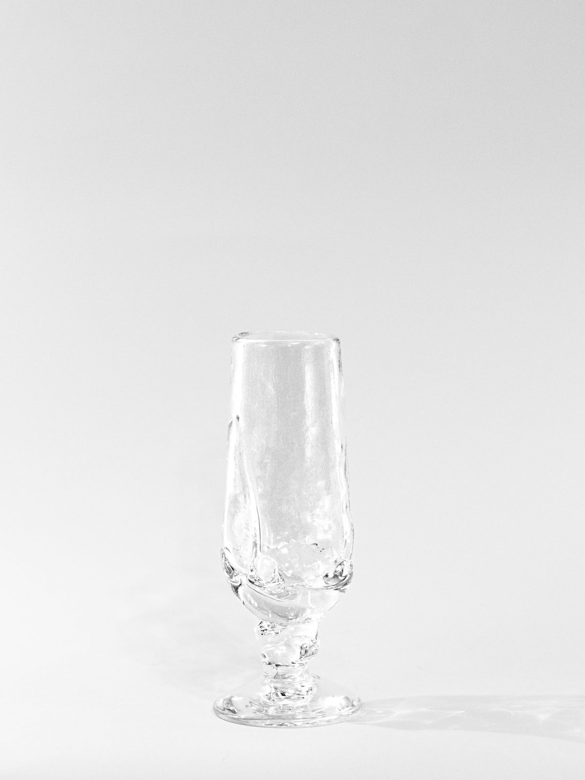 A clear, empty Table Goblet by Szkło Studio stands upright on a white surface with a faint right-side shadow. The simple background highlights the elegance of traditional glass-blowing craftsmanship.