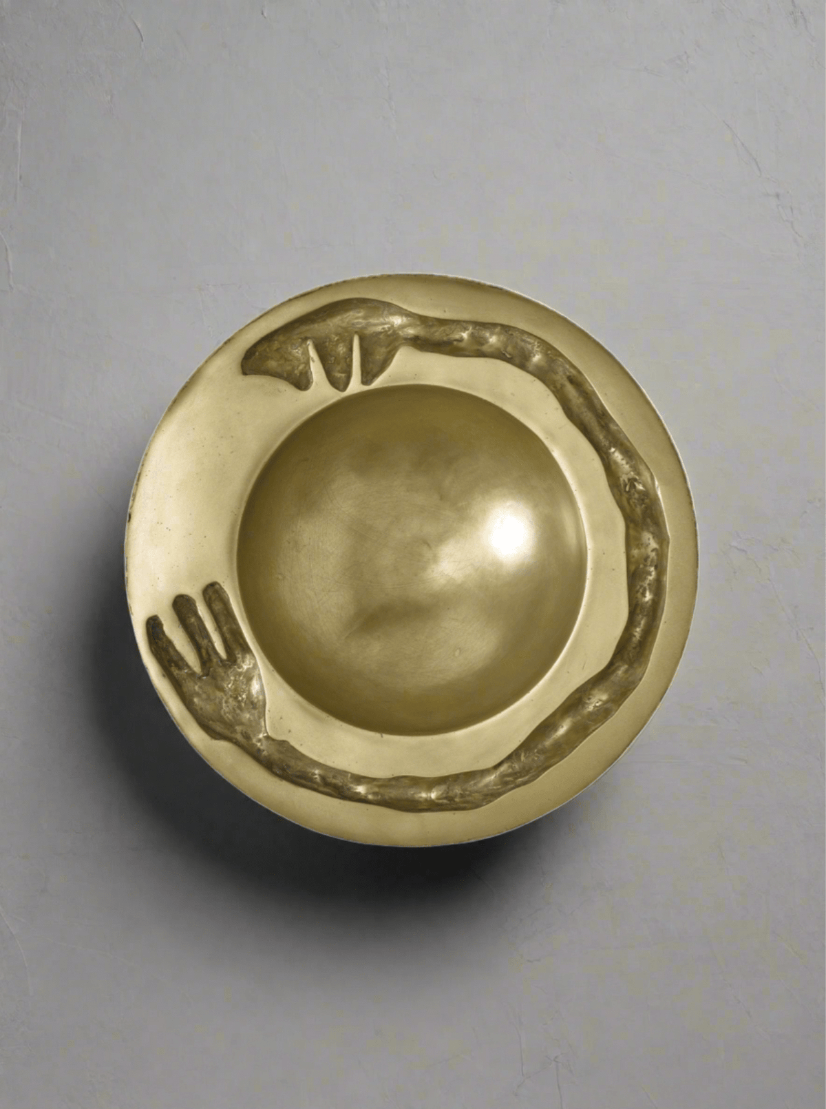 The Signature Dish Brass Sculpture by Lucy Page features a gold-toned, circular bowl with a sculpted snake forming a continuous loop along the raised rim—an eye-catching decorative piece on a smooth, light gray surface.